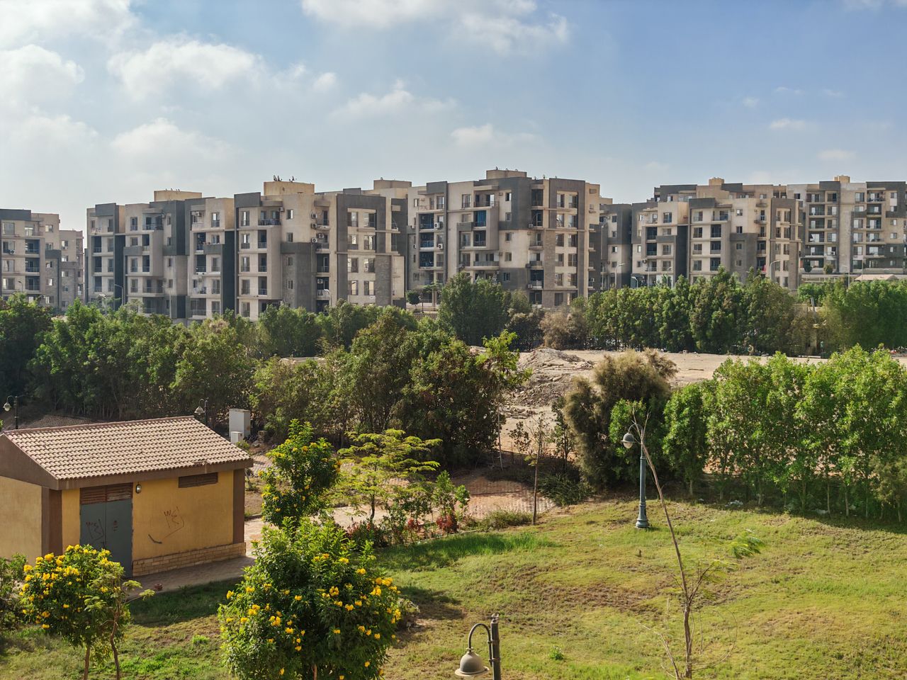View of modern apartment buildings surrounded by greenery under a clear sky.